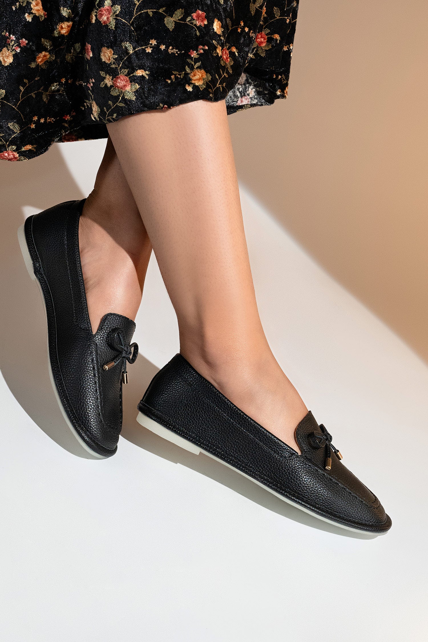 Women's flat moccasin style shoes in black colour and leather texture with matching bow and flexible transparent rubber sole by JULKE.