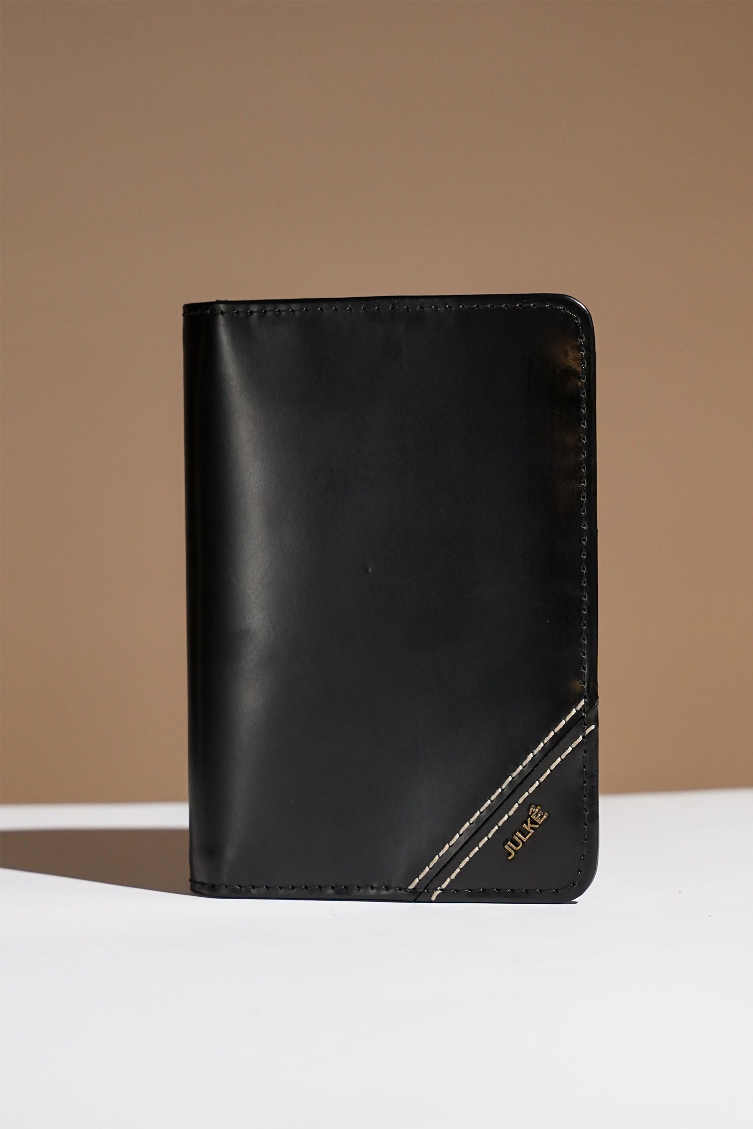 Mens leather bifold passport wallet in black colour with white contrast stitching and metal brand logo by JULKE