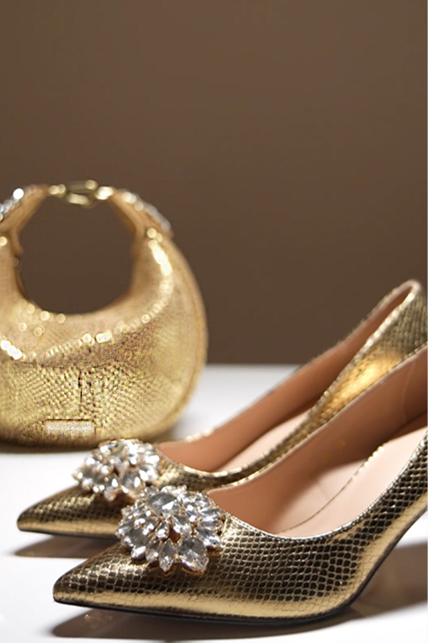 Women's high heel pointed toe pumps and matching leather hand bag in dark gold colour with shiny reptile texture and flower shaped white rhinestone brooch with by JULKE