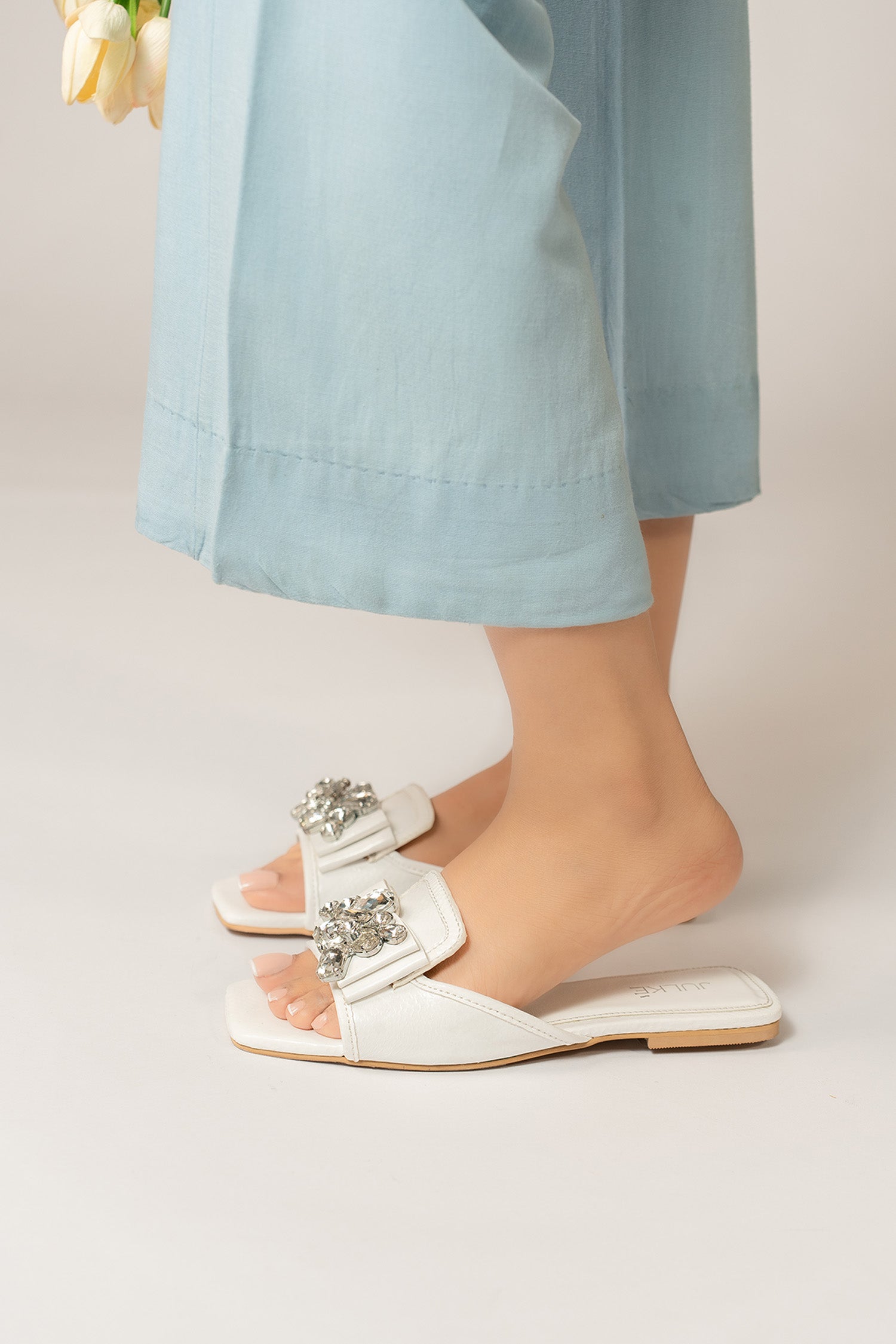 Womens flat slides in white colour with glossy reptile texture and asymmetric rhinestone brooch by JULKE.