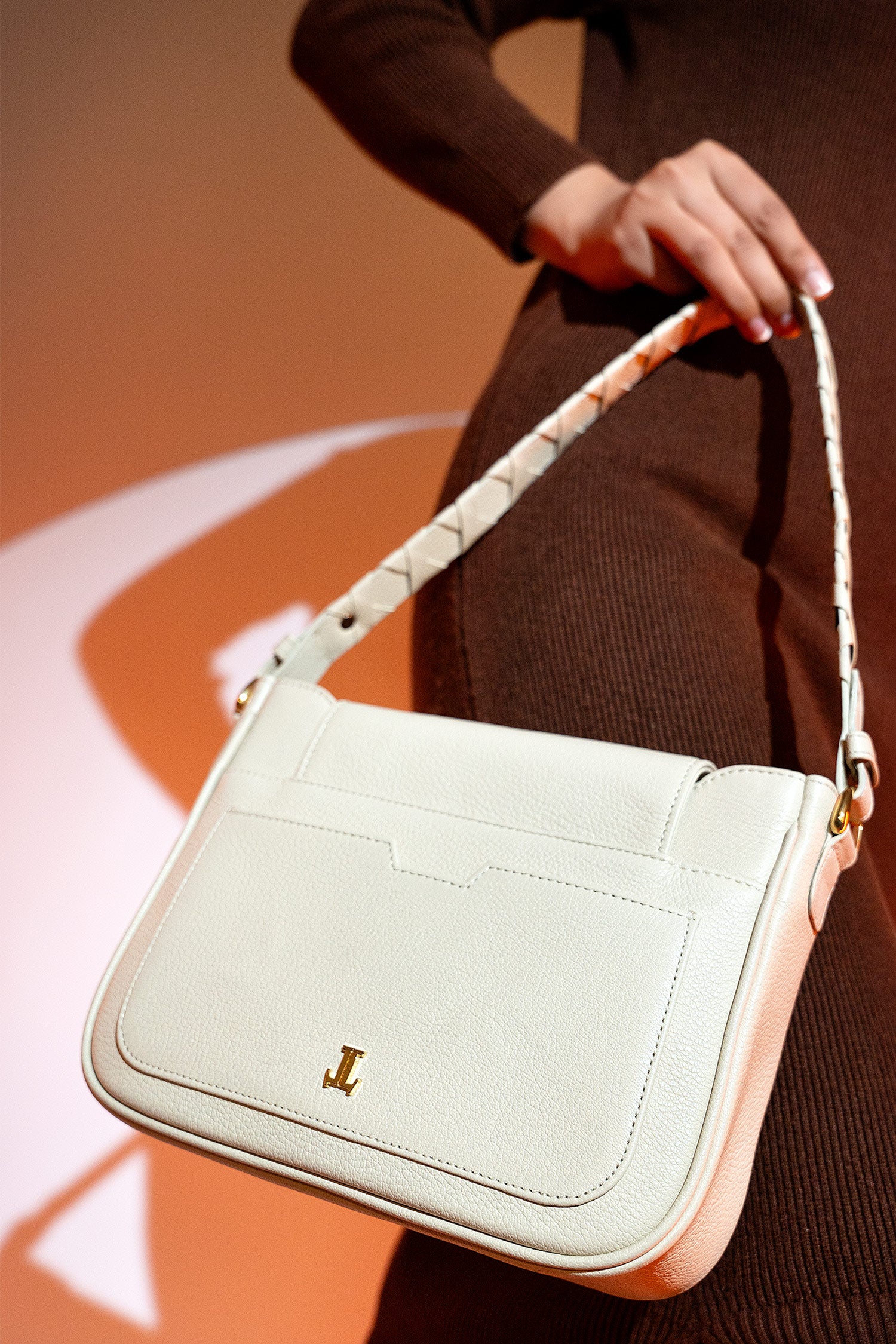 Women's grain texture leather shoulder bag in off white colour with woven shoulder strap and metallic gold doorknocker style buckle by JULKE. 