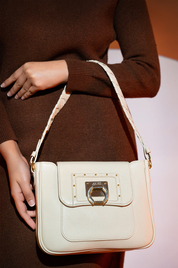 Women's grain texture leather shoulder bag in off white colour with woven shoulder strap and metallic gold doorknocker style buckle by JULKE. 
