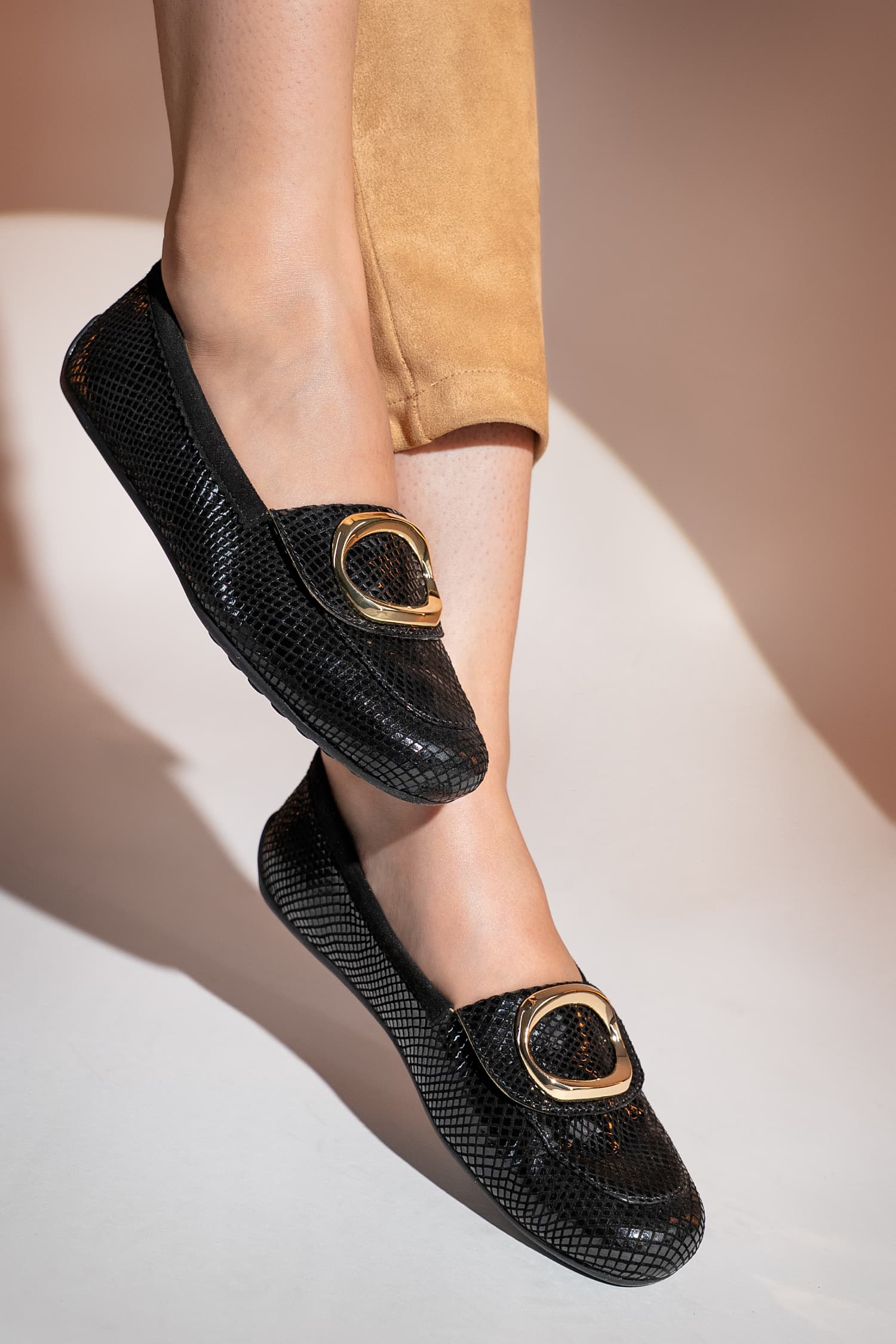 Black loafers with gold buckles worn by a person on a neutral background