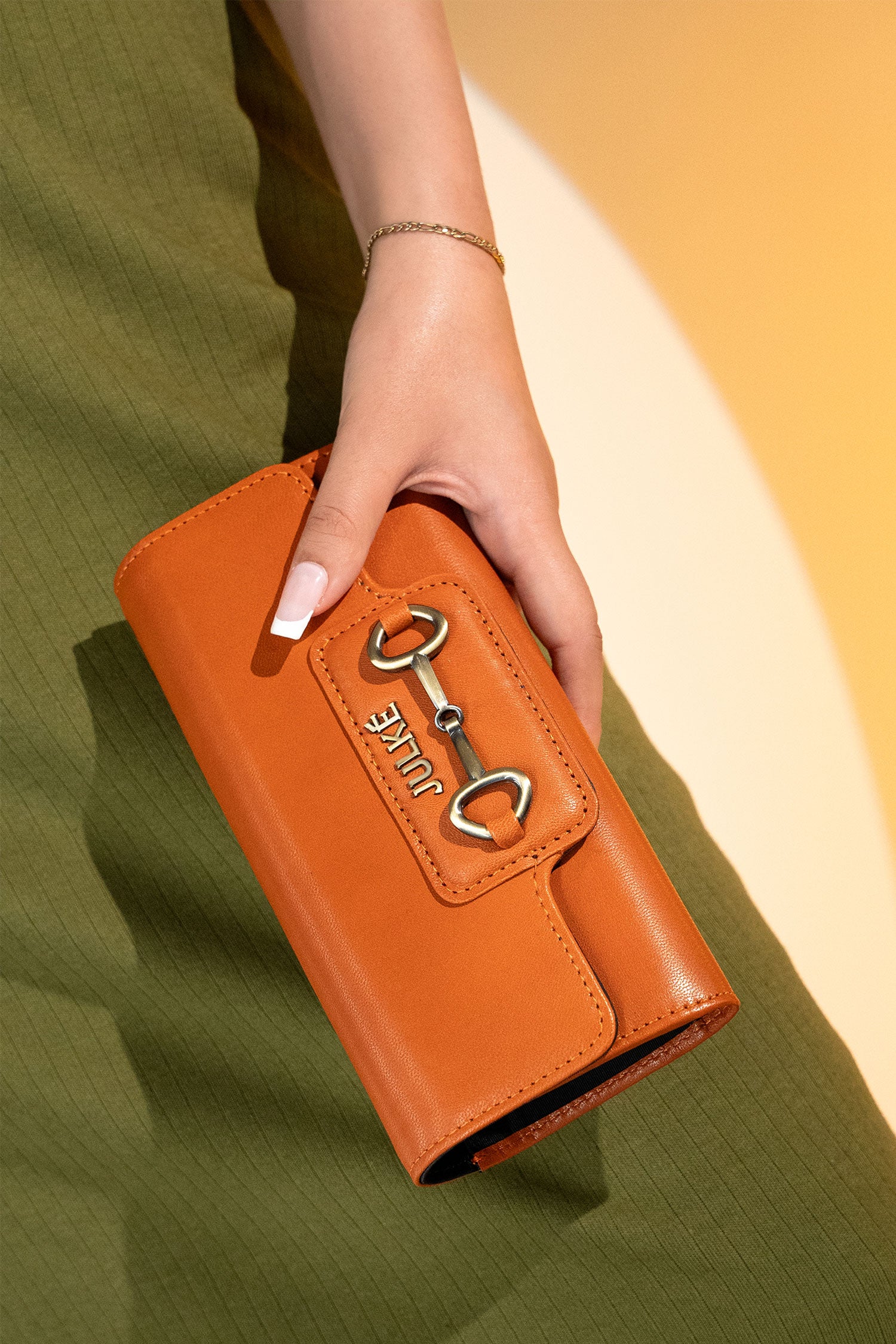 Women's leather long wallet in dark orange colour in envelope shape with long pockets and metallic horse-bit buckle and brand logo by JULKE. 