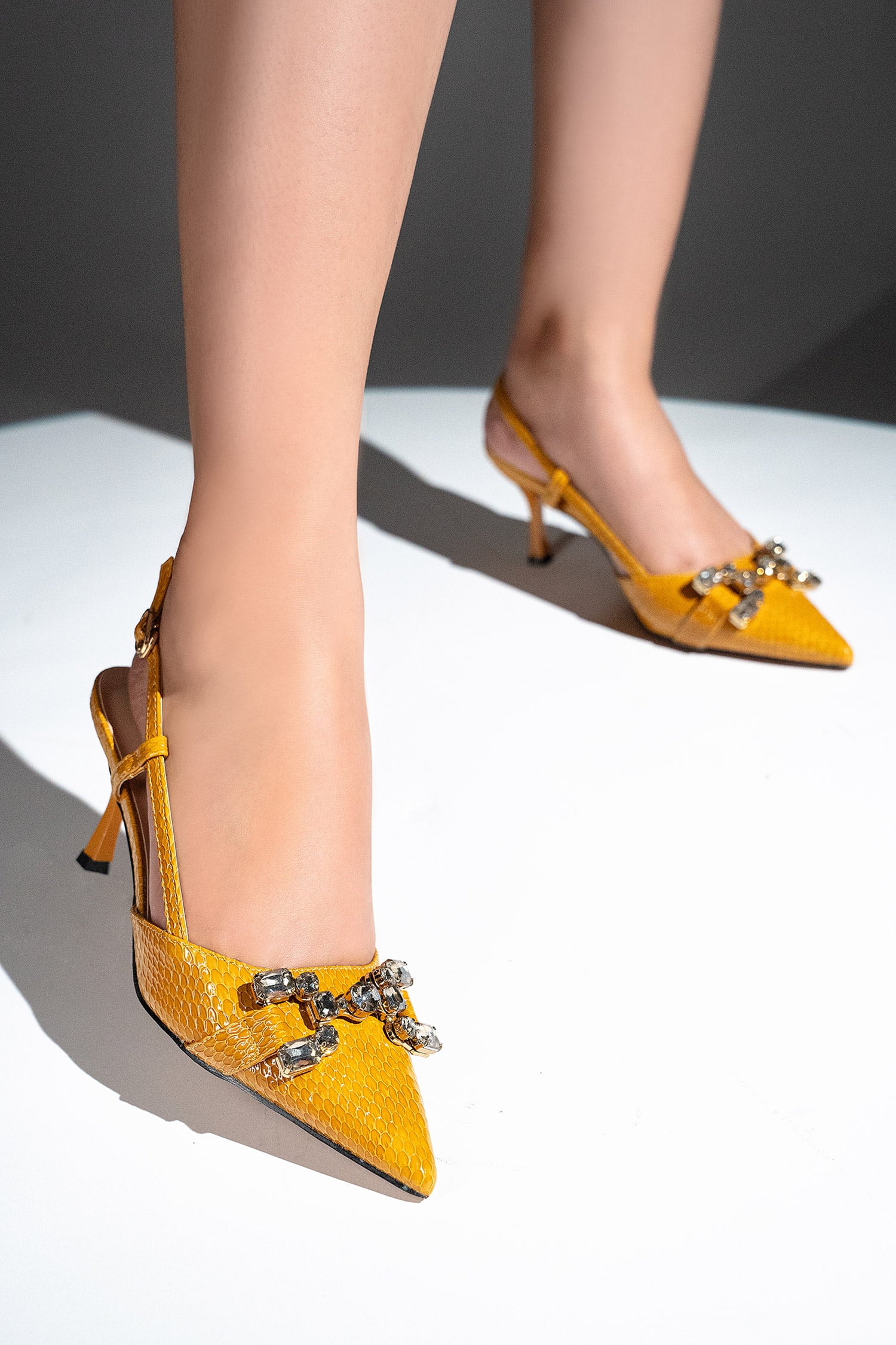 Women's sling back pointed toe heels in mustard yellow colour with glossy dragon scale texture and rhinestone horse-bit buckle by JULKE. 
